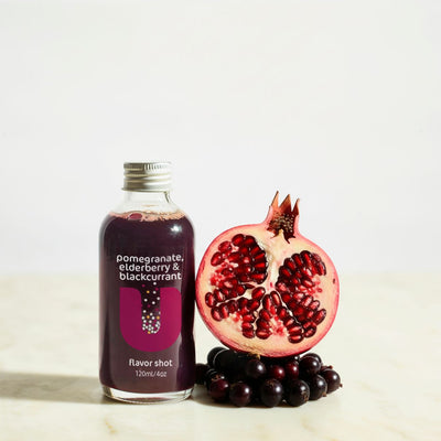 Bottle of pomegranate, blackcurrant flavor shot with a pomegranate and blackberries on a light background