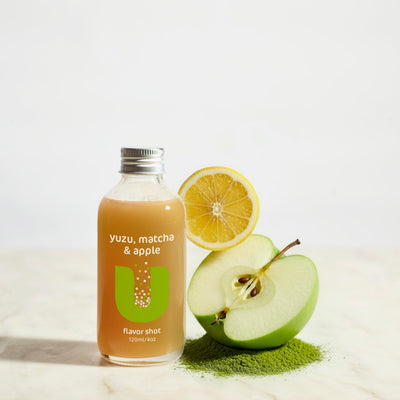 Bottle of yuzu, matcha, and apple flavor shot with a lemon and apple and matcha powder on a light background