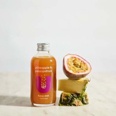 Bottle of pineapple and passionfruit juice with a sliced passionfruit and pineapple on a light background