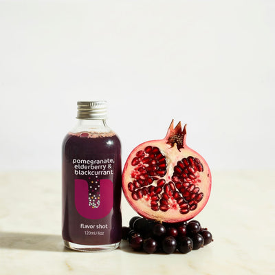 Bottle of pomegranate, blackcurrant flavor shot with a pomegranate and blackberries on a light background