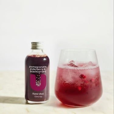 Bottle and glass of pomegranate and blackcurrant flavor shot on a light background