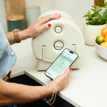 Person using a smartphone app to control a brewing appliance on a countertop.