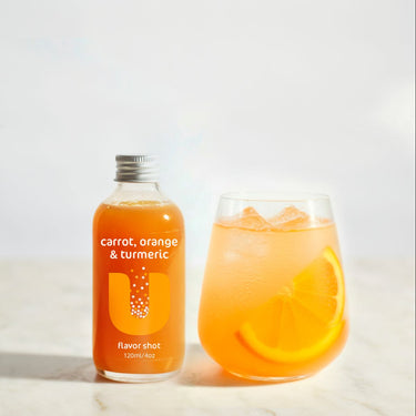 Bottle of 'carrot, orange & turmeric' flavorshot next to a glass of the drink on a white background