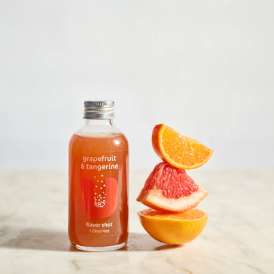 Bottle of grapefruit and tangerine flavor shot with sliced oranges and grapefruit on a marble surface