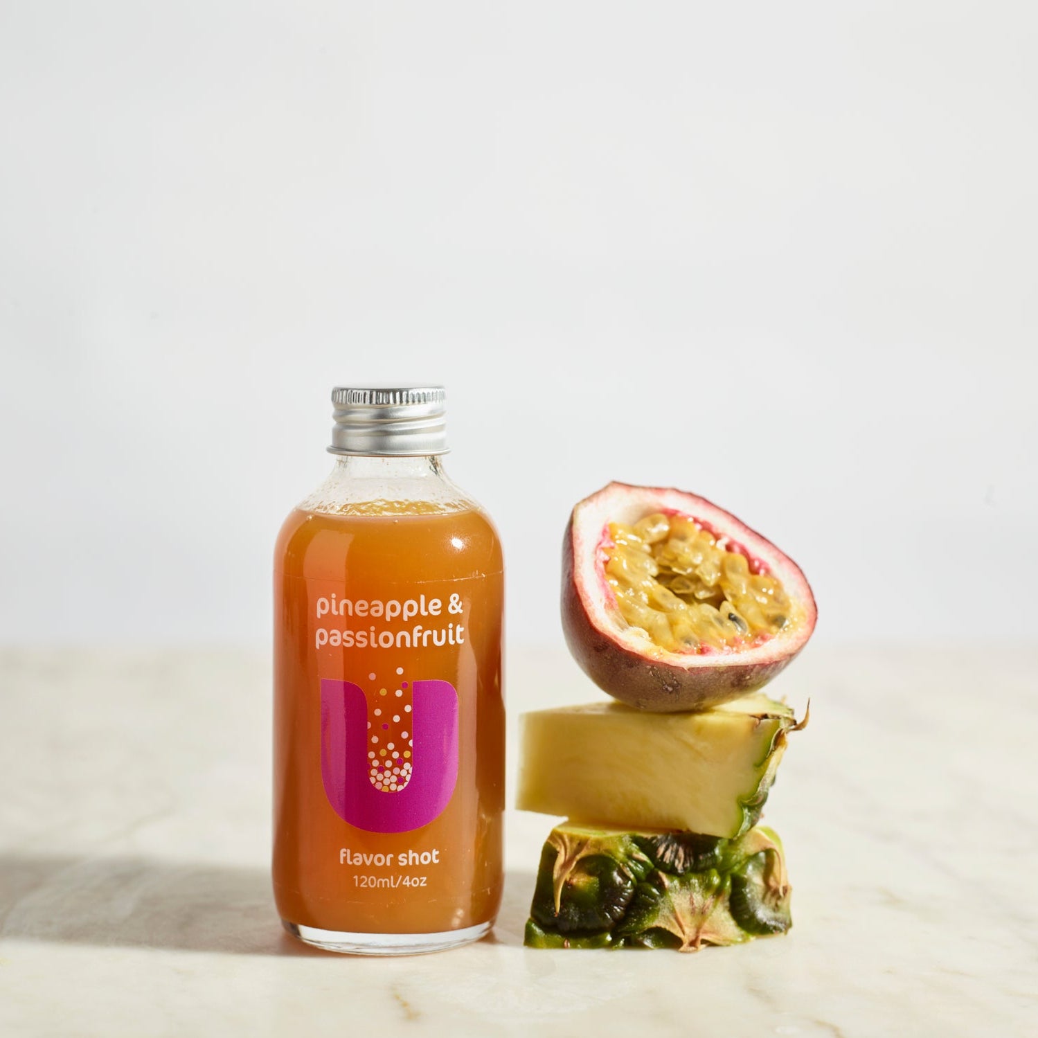 Bottle of pineapple and passionfruit juice with a sliced passionfruit and pineapple on a light background
