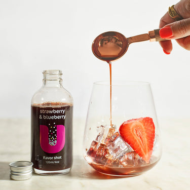 Strawberry and blueberry flavor shot being poured into a glass with ice and a strawberry.