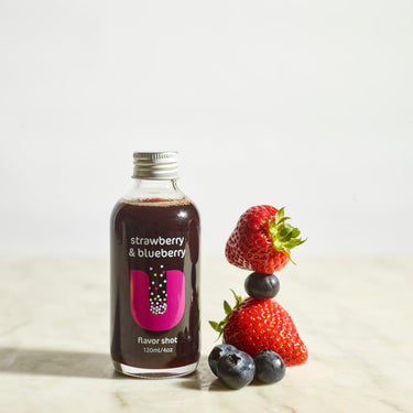 Bottle of strawberry and blueberry flavor shot with fresh strawberries and blueberries on a light background