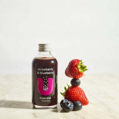 Bottle of strawberry and blueberry flavor shot with fresh strawberries and blueberries on a light background