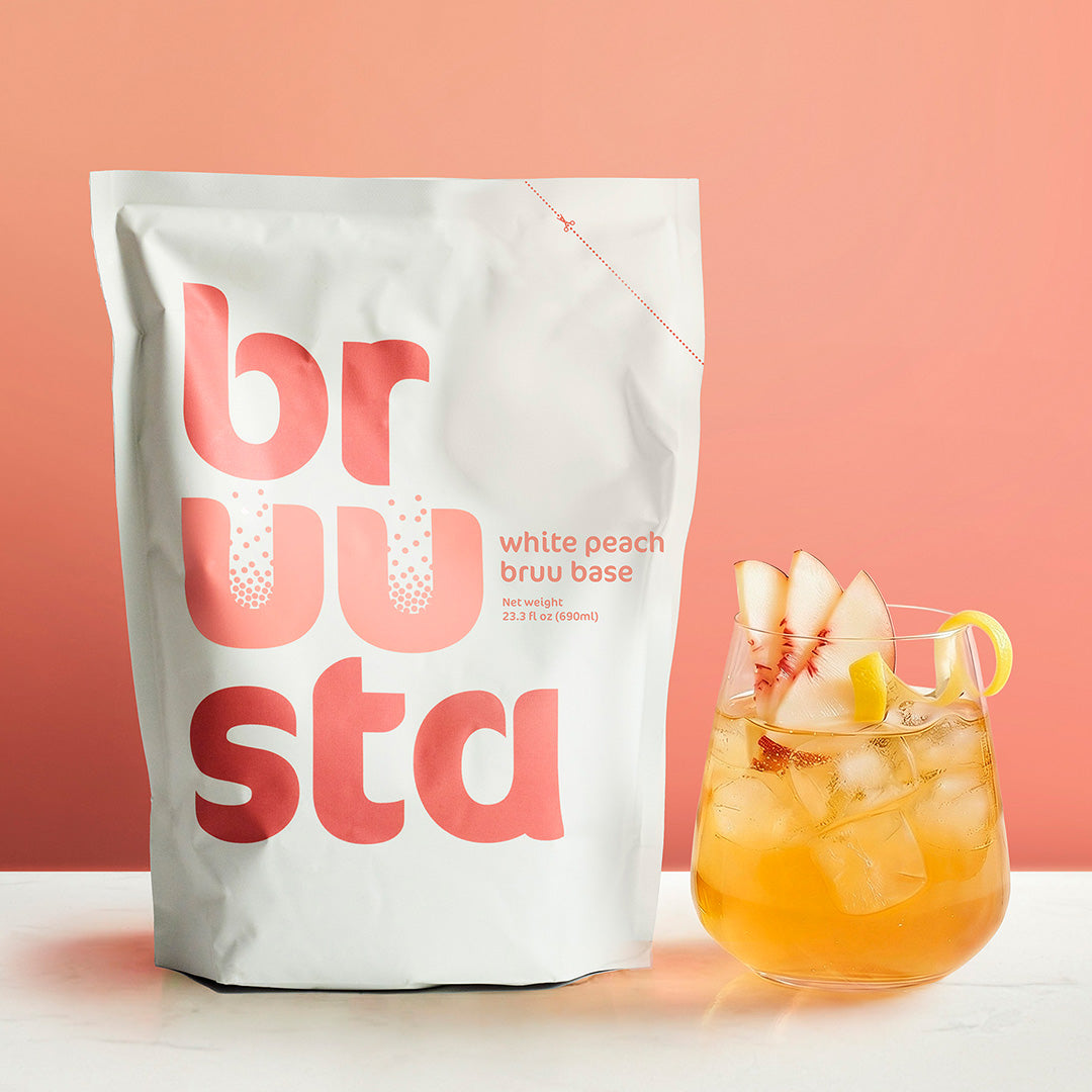 Brusta white peach bruu base package with a peach-themed cocktail on a pink background