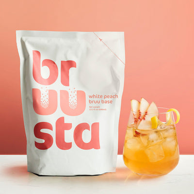 Brusta white peach bruu base package with a peach-themed cocktail on a pink background